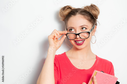 Fototapeta Naklejka Na Ścianę i Meble -  the portrait of young blondie caucasian woman with two hair bundles, glasses for vision, braces smiling widely and holding some notebooks; young woman businessman concept 