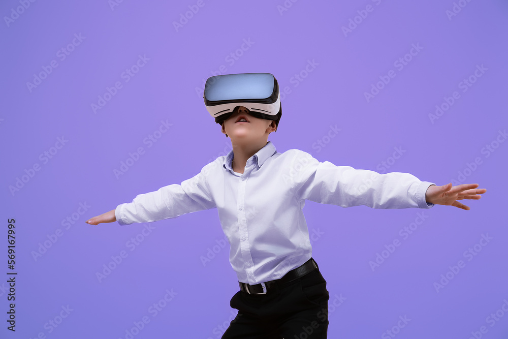 Schoolboy plays video game while using VR headset on purple background. Child in virtual goggles. Schoolboy plays video game while using VR headset on purple background. Child in virtual goggles.