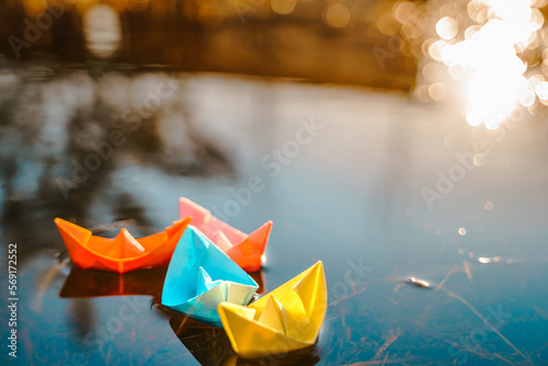 Multicolored paper boats. Colorful pink yellow blue orange ships in big spring snow puddle on winter street. Warm wet rainy weather, old grass. Hello spring, autumn. Children play, have fun outdoors