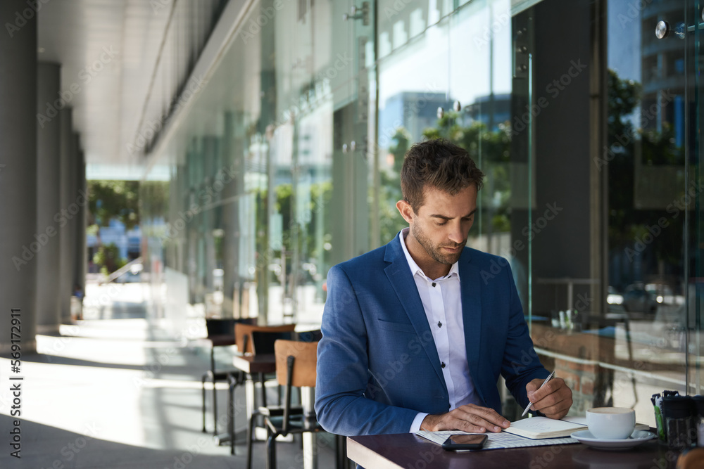 Businessman sitting at a cafe table writing in a notebook Businessman sitting at a cafe table writing in a notebook