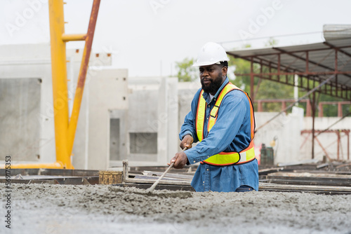 Construction worker uses long steel trowel spreading wet concrete pouring at precast concrete wall construction site. Worker or mason working or making smooth surface of concrete with equipment tool