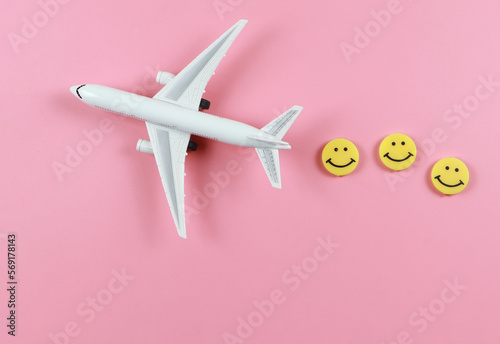 flat lay of airplane model with three yellow circle smiling faces on pink background. Happy or fun trip concept.