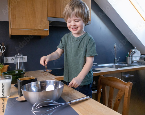 The boy prepares the dough from eggs, sugar, sour cream and flour by himself in the kitchen photo