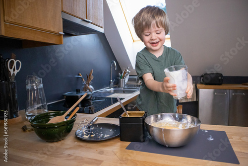 The boy prepares the dough from eggs, sugar, sour cream and flour by himself in the kitchen photo