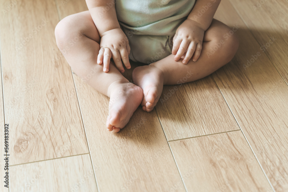 Baby sits on a wooden laminate floor. Bare legs and feet of a baby in the living room floor Baby sits on a wooden laminate floor. Bare legs and feet of a baby in the living room floor