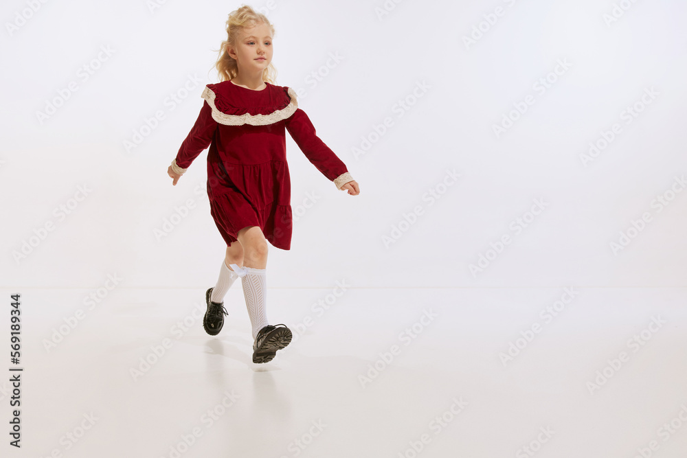 Portrait of charming little girl, kid in retro dress isolated over white studio background. Concept of childhood, kids fashion, lifestyle, education, friendship.