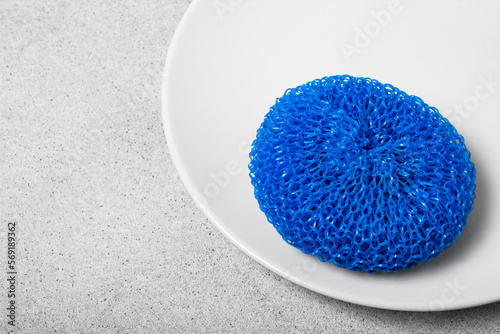 Colorful plastic scourer on a white plate on a light neutral background. Gentle dishwashing. House cleaning.