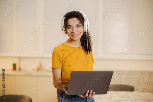 Close up portrait of indian or arabian woman inside home with headset for video call, woman smiling and looking at camera, couch customer support tech helpline.