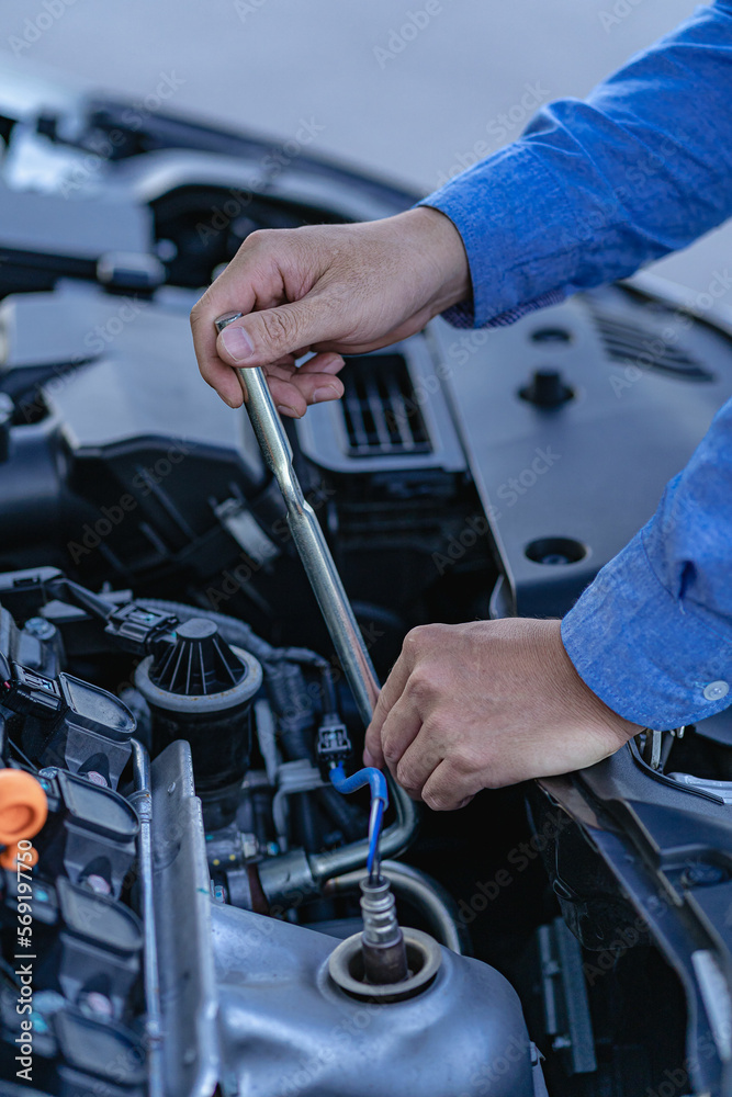 Man inspecting and fixing his car using wrench while working on broken engine on road Car service and maintenance checks vertical image Man inspecting and fixing his car using wrench while working on broken engine on road Car service and maintenance checks vertical image