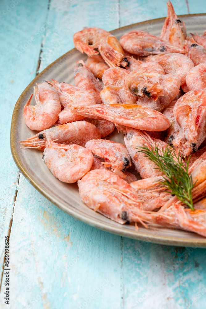 Plate with frozen shrimp on a wooden background. Vertical photo Plate with frozen shrimp on a wooden background. Vertical photo