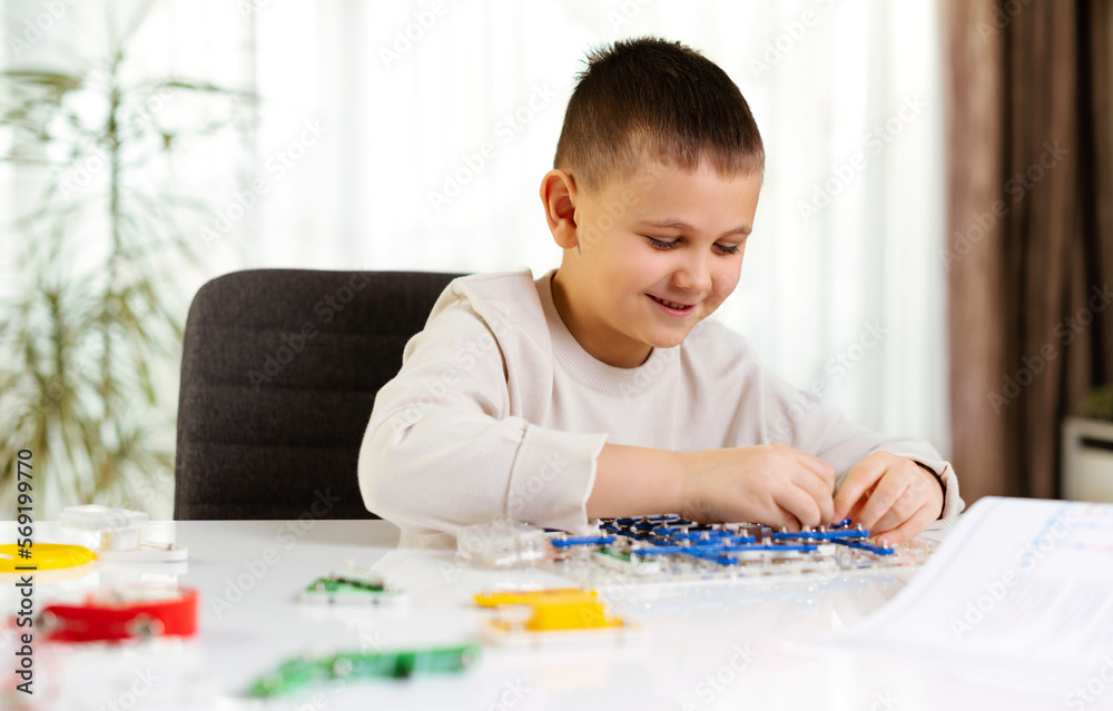 Primery school boy plays with an electronic constructor at home at the desk. Future engineer study to compose electronic circuits. Creative hobby. New skills Primery school boy plays with an electronic constructor at home at the desk. Future engineer study to compose electronic circuits. Creative hobby. New skills
