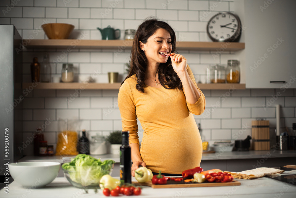 Young woman in kitchen. Beautiful pregnant woman making salad..