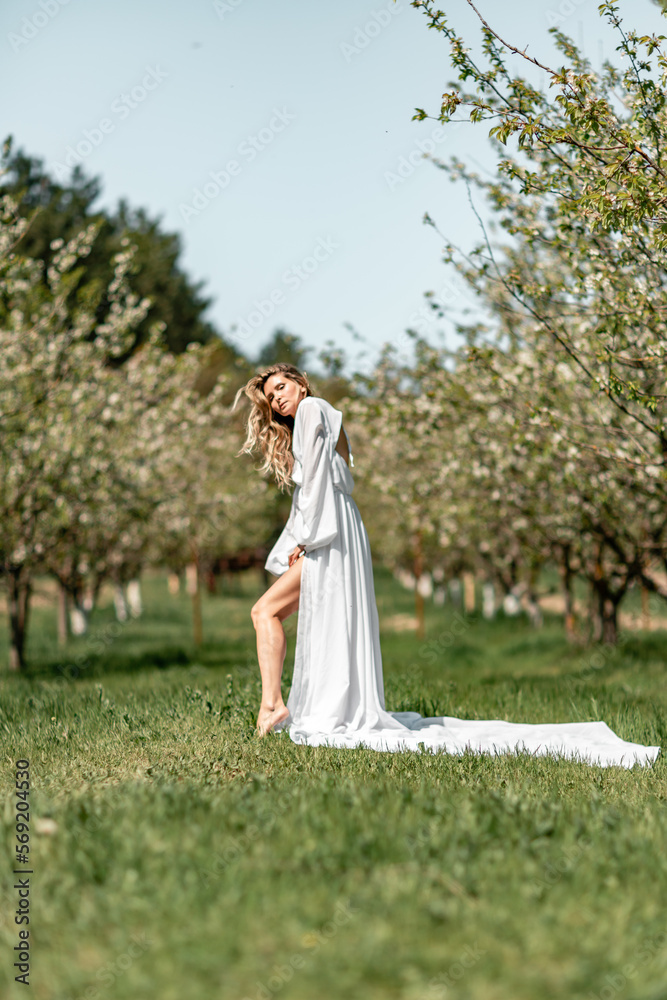 Blond blooming garden. A woman in a white dress walks through a blossoming cherry orchard. Long dress flies to the sides, Blond blooming garden. A woman in a white dress walks through a blossoming cherry orchard. Long dress flies to the sides,