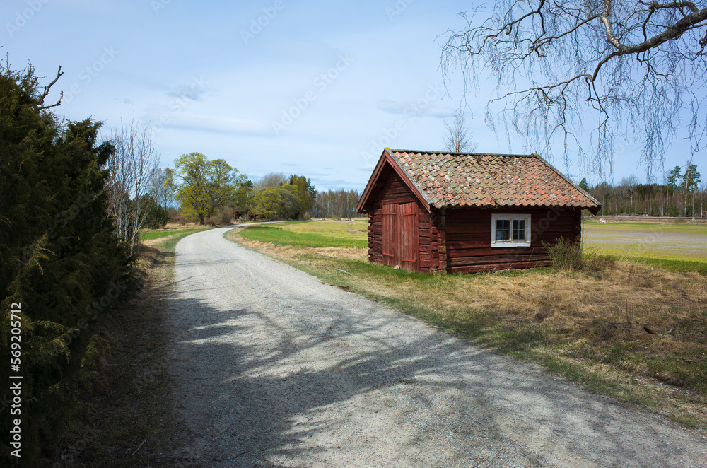 Rural Sweden, Old traditional red wooded house next to the gravel road in countryside spring in Scandinavia