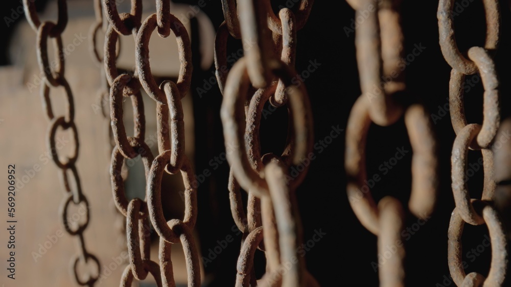 Rusty metal old chain dangling in dark indoor space. Close up of the links of an aged iron chain covered with corrosion and dust. Rough damaged metal structure. Grunge. Strong uneven metal connections Rusty metal old chain dangling in dark indoor space. Close up of the links of an aged iron chain covered with corrosion and dust. Rough damaged metal structure. Grunge. Strong uneven metal connections