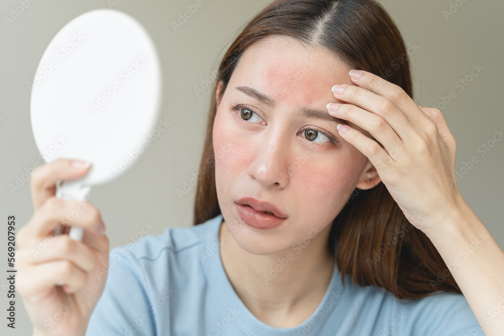 Sensitive skin with cosmetology, Asian young woman looking at red spot on her face from cosmetic allergy in the mirror. Sensitive skin with cosmetology, Asian young woman looking at red spot on her face from cosmetic allergy in the mirror.
