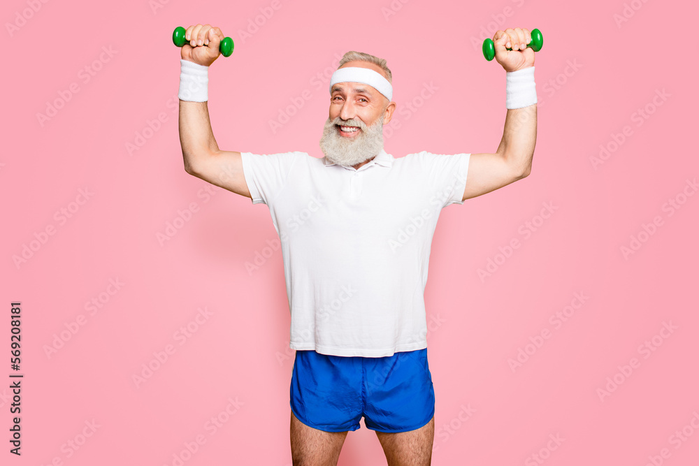 Fototapeta premium Body care, hobby, weight loss lifestyle. Cheerful cool grandpa with humor grimace exercising holding equipment up, lifts it with strength and power, wearing blue sexy shorts, so hot
