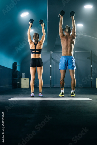 Rear view of muscular man and woman doing exercise in gym with dumbbell.