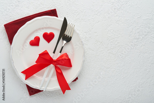Valentines day romantic table setting. Empty or closeup of a dinner black plate, knife, fork and decorative silk hearts on white background. Holiday concept. Copy space for inscriptions.