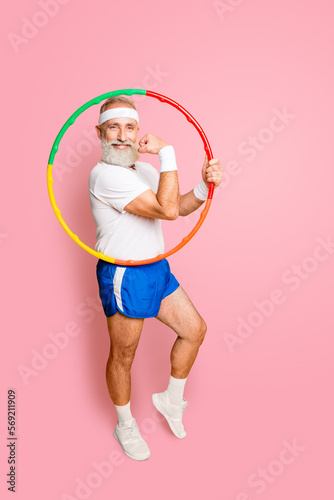 Cheerful cool excited crazy funny fooling playful gymnast grandpa with comic grimace shows off with hoolahoop, demonstrating his bicep. Body care, hobby, weight loss © deagreez