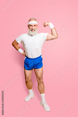 Full length of cheerful excited mature goofy cool pensioner grandpa champion practising bodybuilding, showing off his pumped hand. Body care, strength, leadership, motivation lifestyle