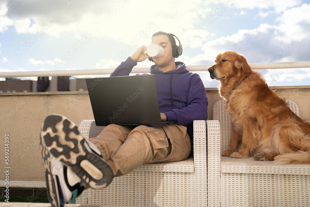 Serious man drinking coffee and working on laptop with dog Serious man drinking coffee and working on laptop with dog