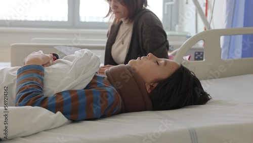 Preteen child, boy, lying in hospital with fractured thoracic spine, vertebralis, mother sitting next to his bed photo