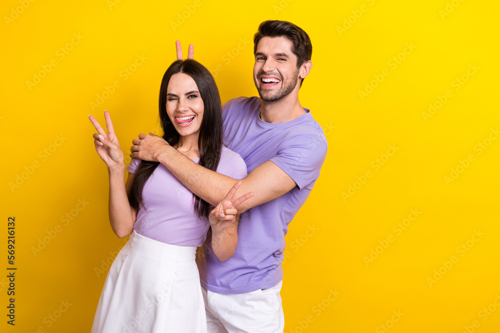 Obraz premium Photo of two idyllic positive carefree people hug show v-sign make horns isolated on yellow color background