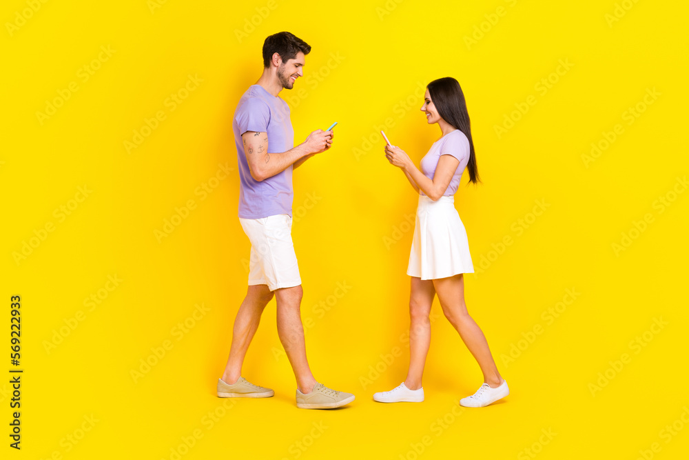 Full body photo of pretty young girl male texting gadget walk meeting dressed stylish violet clothes isolated on yellow color background