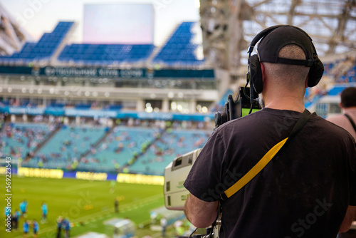 Rear view of an experienced video operator wearing headphones with a professional camera during a football match. Professional sports media at the stadium during a game of football