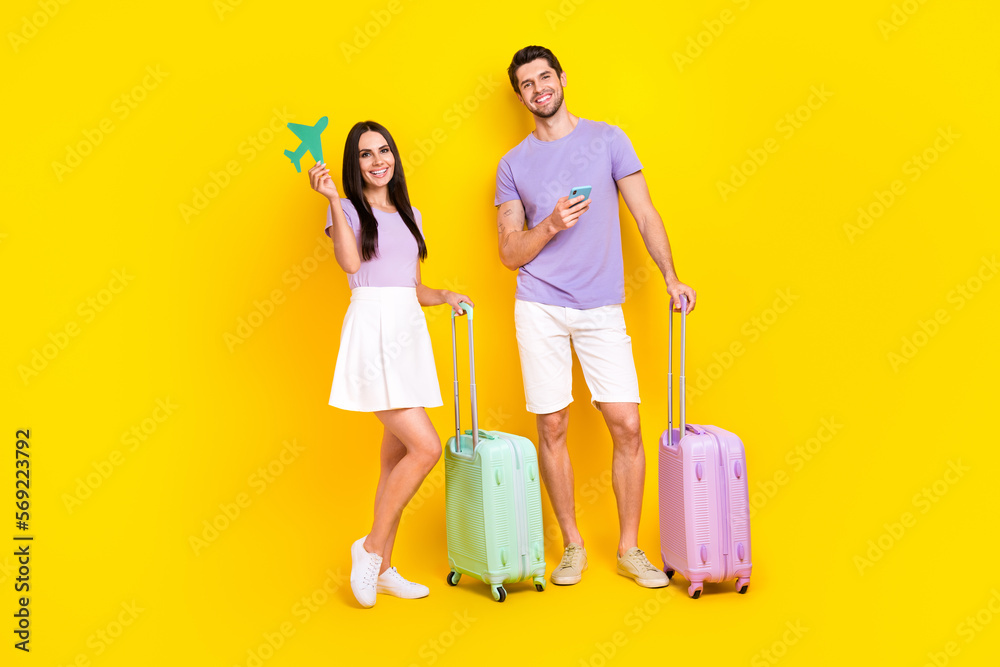 Full size photo of attractive woman man paper plane suitcase device booking dressed stylish violet look isolated on yellow color background Full size photo of attractive woman man paper plane suitcase device booking dressed stylish violet look isolated on yellow color background