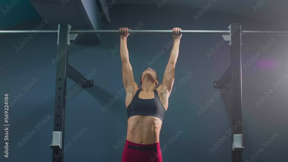 Young fit woman in sportswear doing pull ups at gym.