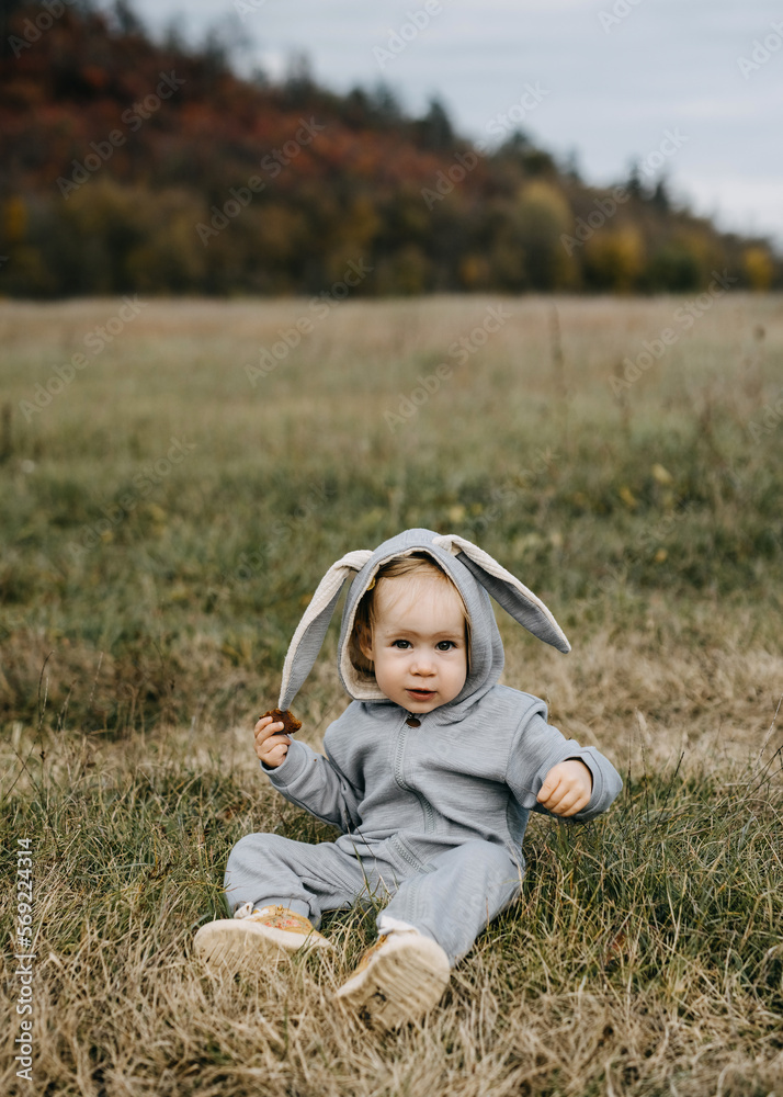 Little child in a grey bunny costume sitting on grass in an open field. Little child in a grey bunny costume sitting on grass in an open field.