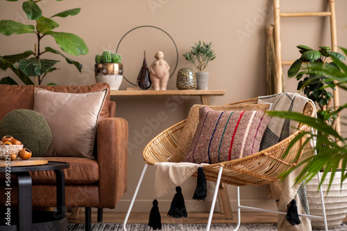 Quadro su tela Interior design of living room interior with brown sofa, braided armchair, patterned pillows, round coffee table, stylish sculpture, plant in flowerpot and personal accessories