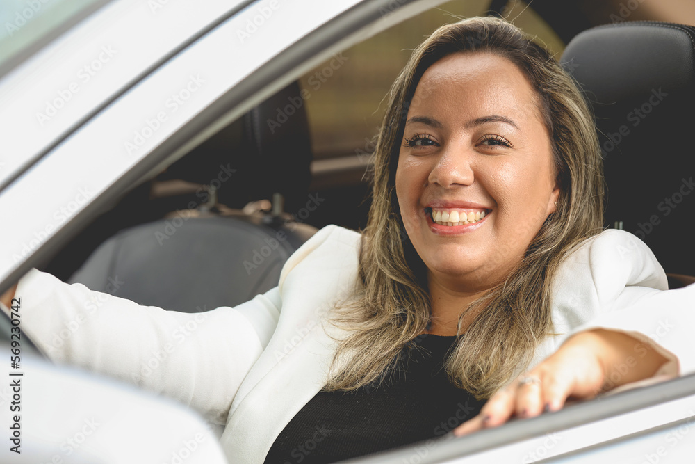 Uma mulher como motorista dentro de um carro de cor prata que está muito feliz e sorrindo para a câmera. Pessoa, Transporte, Veículo. - obrazy, fototapety, plakaty 