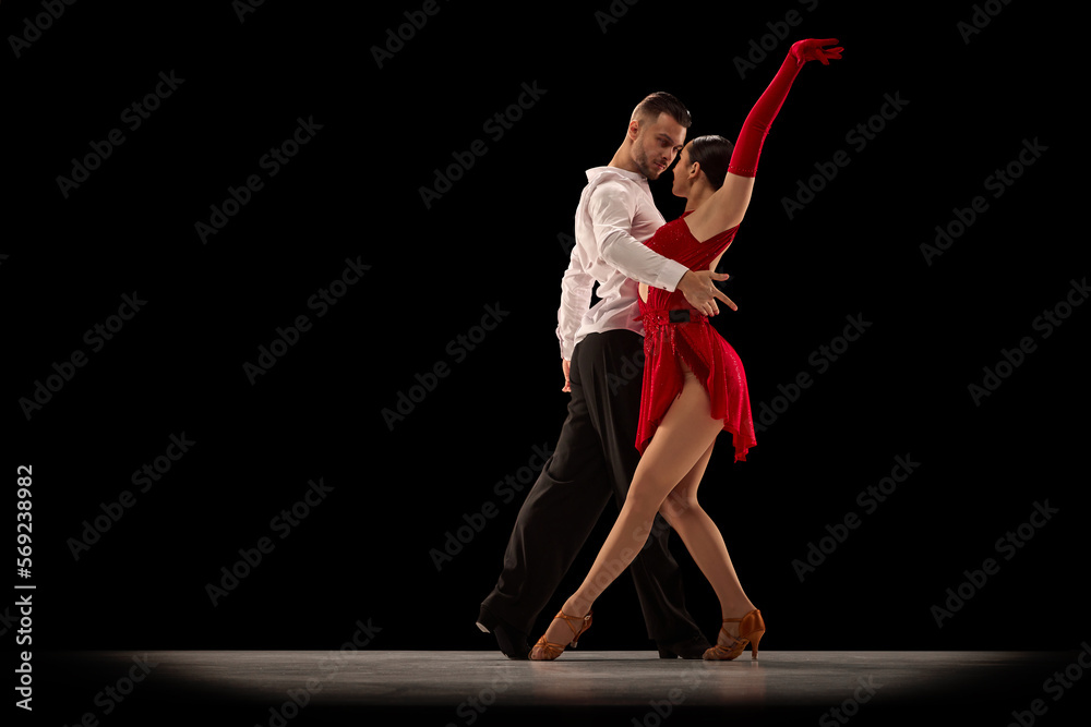 Passionate attractive young man and woman, professional ballroom dancers dancing tango over black background. Concept of hobby, lifestyle, action, beauty of movements, emotions, fashion, art - obrazy, fototapety, plakaty 