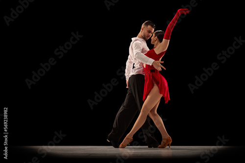 Passionate attractive young man and woman, professional ballroom dancers dancing tango over black background. Concept of hobby, lifestyle, action, beauty of movements, emotions, fashion, art photo