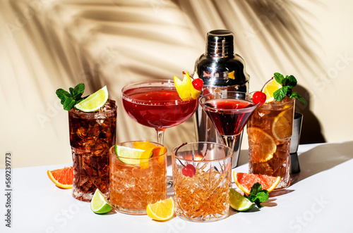 Summer alcoholic cocktails: rum cola, long island ice tea, manhattan, cosmopolitan, old fashioned - trendy popular drinks for cocktail party. Beige background, hard light, palm leaves shadow