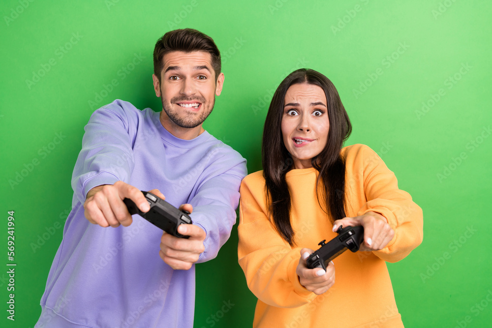 Portrait of two excited people biting lips try hard playing video games isolated on green color background Portrait of two excited people biting lips try hard playing video games isolated on green color background