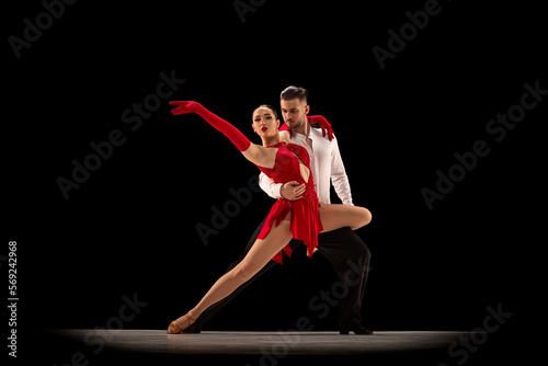 Passionate attractive young man and woman, professional ballroom dancers dancing tango over black background. Concept of hobby, lifestyle, action, beauty of movements, emotions, fashion, art