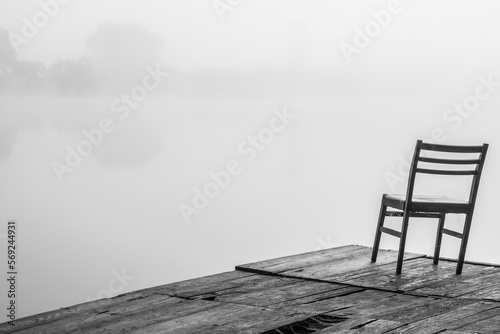 chair on the pier on the shore of the lake in foggy weather. Black and white image.