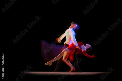 Fototapeta Naklejka Na Ścianę i Meble -  Man and woman, professional dancers performing ballroom, tango over black background with mixed neon lights. Concept of hobby, lifestyle, action, beauty of movements, emotions, fashion, art