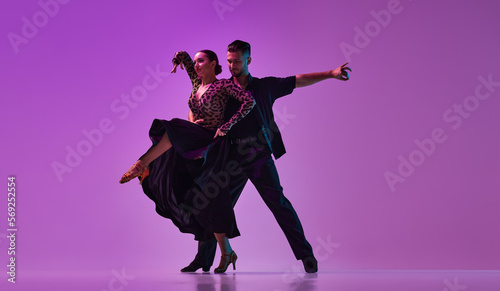 Talented young man and woman, professional dancers performing tango over purple background on neon lights. Concept of hobby, lifestyle, action, beauty of movements, emotions, fashion, art