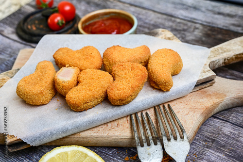  Crispy oven baked chicken nuggets and ketchup. Breaded chicken fillets with chilly peppers and fresh basi on wooden rustic background