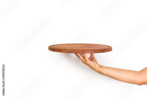 Mano de mujer sosteniendo un plato redondo de madera sobre un fondo blanco liso y aislado. Vista de frente y de cerca. Copy space