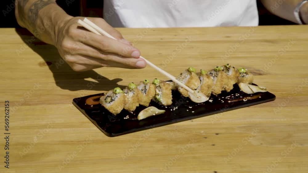 Persona bañando en salsa inglesa y comiendo un Delicioso plato de sushi empanizado bañado en salsa inglesa sobre una mesa de madera al atardecer