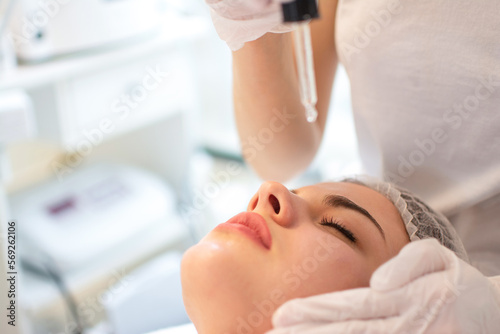 Beautician holding pipette and applying serum on face of woman in spa salon