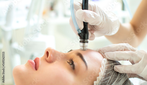 Closeup shot of young woman receiving microdermabrasion therapy on forehead at beauty spa