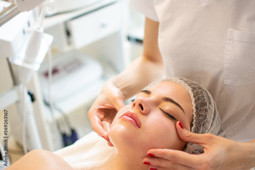 Close up of beautiful young woman having curative facial cheeks massage in beauty salon. Close up of beautiful young woman having curative facial cheeks massage in beauty salon.