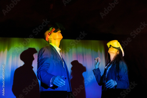 Female and male colleagues watching through virtual reality glasses in illuminated exhibition center